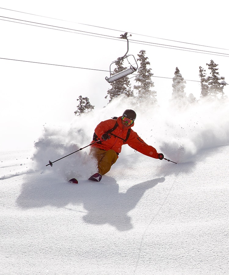 Base Mountain Sports skier skiing down a snowy mountain in Colorado with ski lift in background